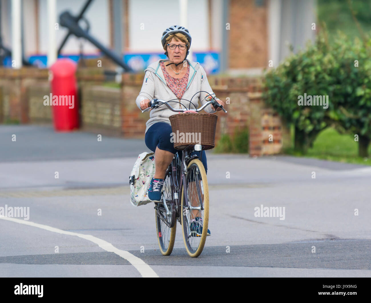 Ältere Frau auf einem Fahrrad mit Korb und trug einen Helm. Dame auf einem Rad in einem fahrradhelm. Stockfoto