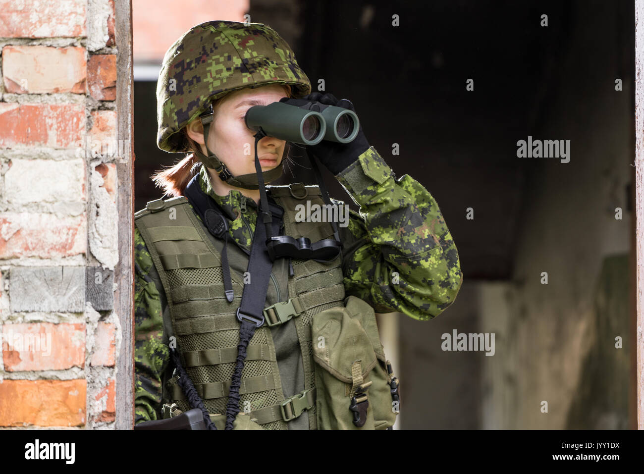 Portrait von bewaffneten Frau mit Camouflage. Junge weibliche Soldaten mit dem Fernglas beobachten. Kind Soldat mit Gewehr im Krieg, Haus Ruinen Hintergrund. Militar Stockfoto