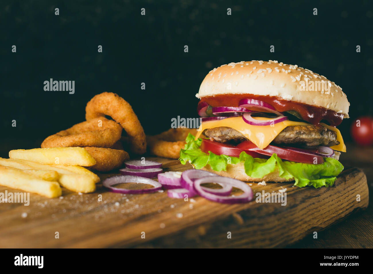 Cheeseburger, Pommes frites und Zwiebelringe auf Holz Schneidebrett über Holz- Hintergrund. Detailansicht, selektive konzentrieren. Fast food Konzept Stockfoto