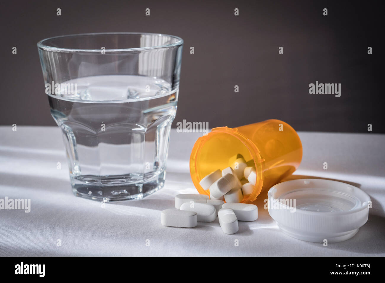 Einige Pillen unterschiedlicher Größe und Farbe zusammen mit einem Glas Wasser Stockfoto