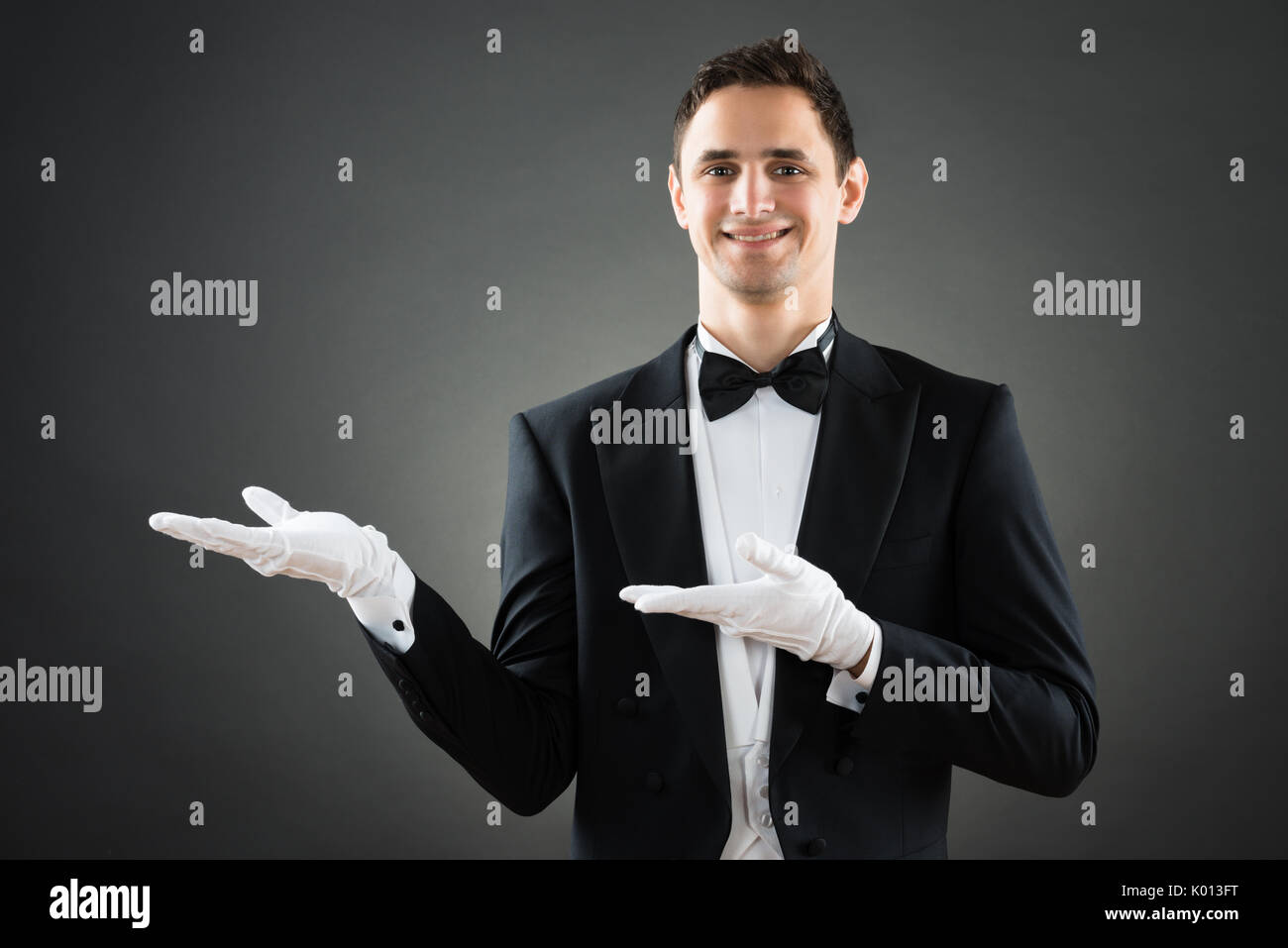 Portrait von zuversichtlich Kellner Präsentation unsichtbare Produkt gegen grauer Hintergrund Stockfoto