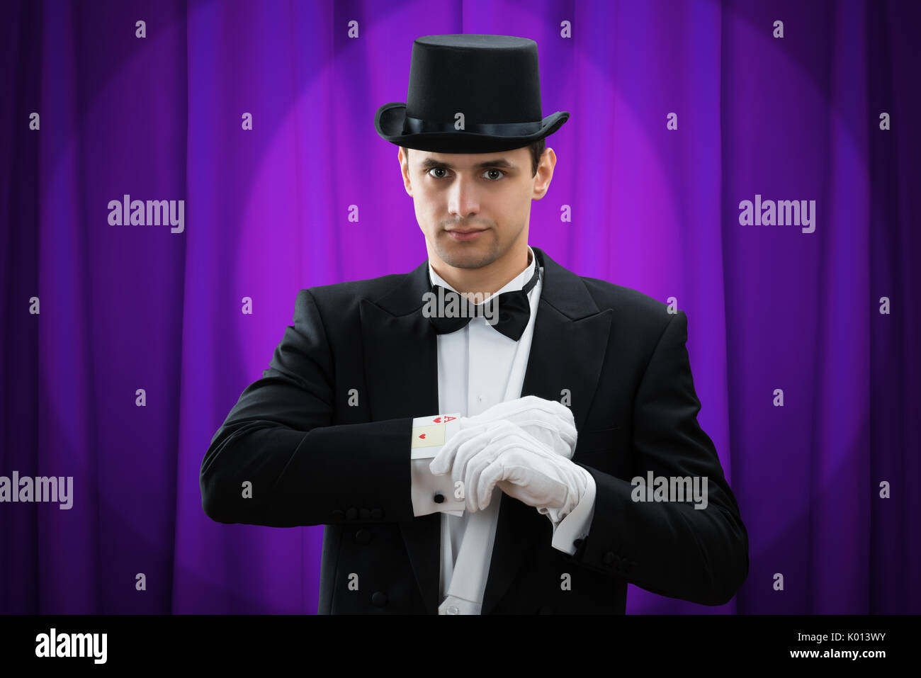 Portrait von jungen männlichen Zauberer zugesehen magic Trick mit Karten gegen lila Vorhang Stockfoto