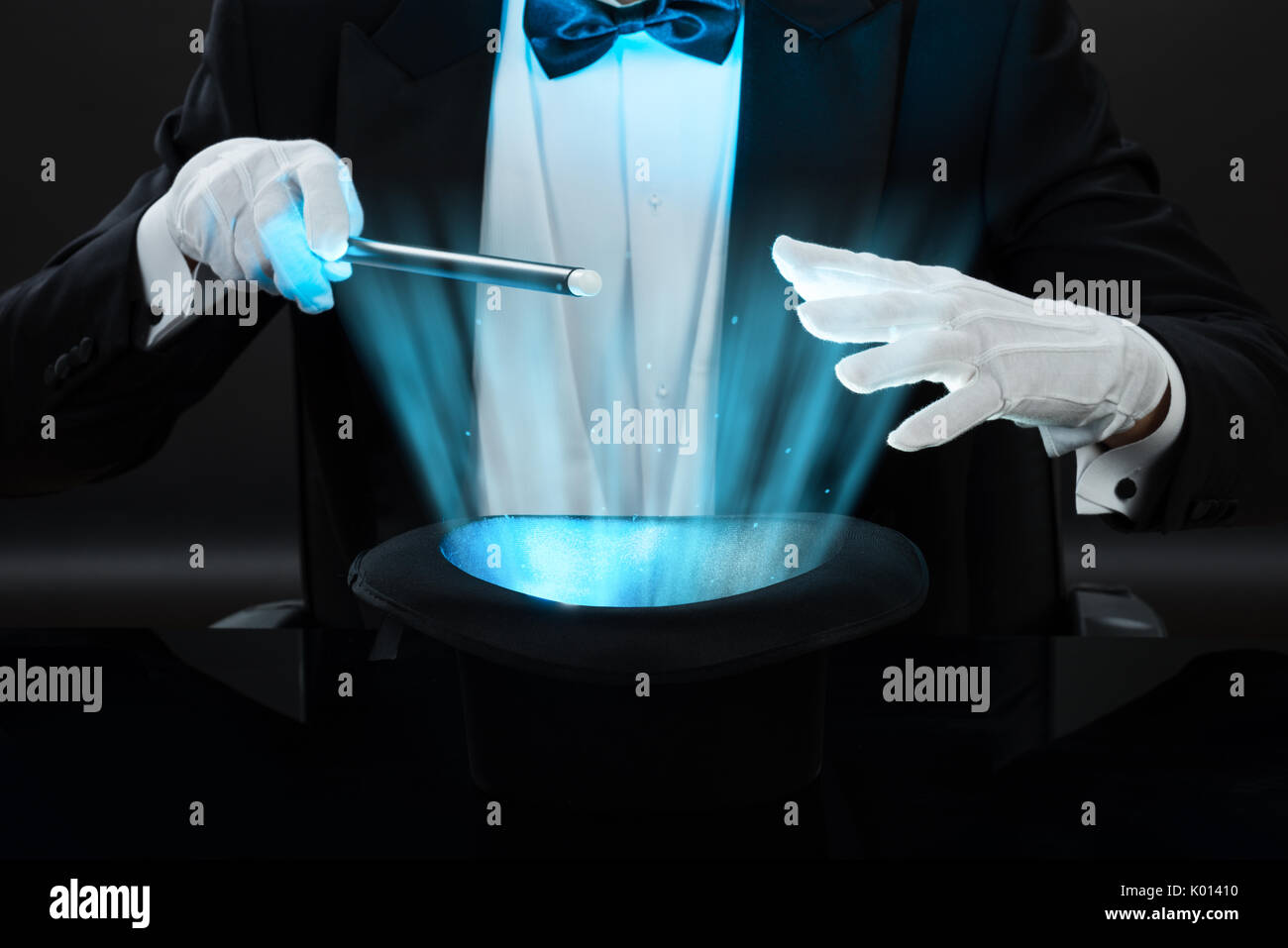 Mittelteil der Zauberer mit Zauberstab über beleuchtete Hut auf schwarzem Hintergrund Stockfoto