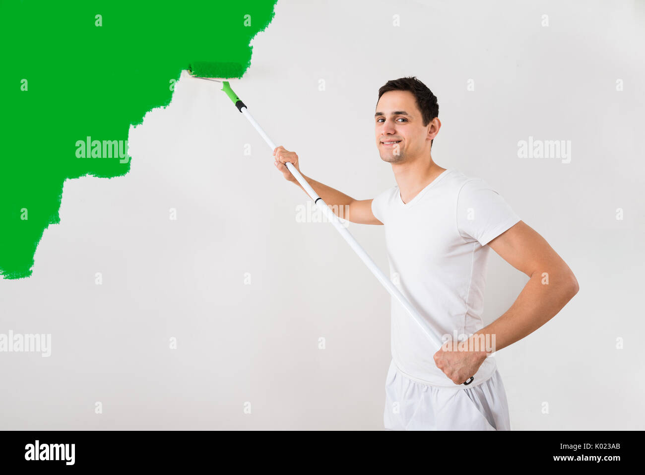 Junger Mann Malerei Wand mit grüner Farbe Roller zu Hause Stockfoto