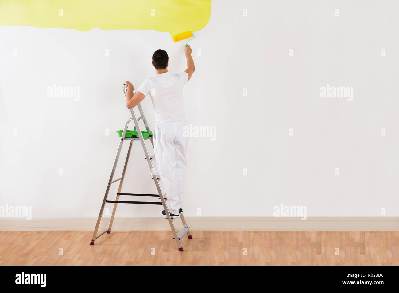 Ansicht der Rückseite des jungen Mannes Malerei Wand mit gelber Farbe Roller zu Hause Stockfoto