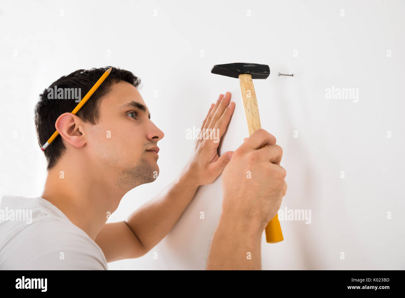 Seitenansicht des jungen Mannes hämmern Nagel auf weisse Wand zu Hause Stockfoto