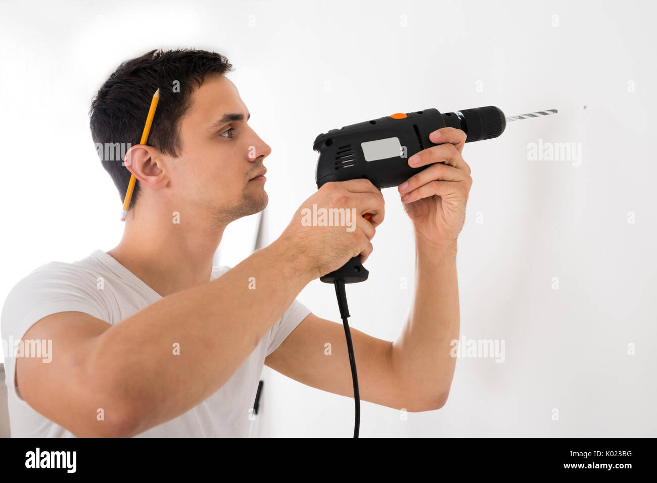 Junger Mann mit Bohrmaschine auf weißer Wand zu Hause Stockfoto
