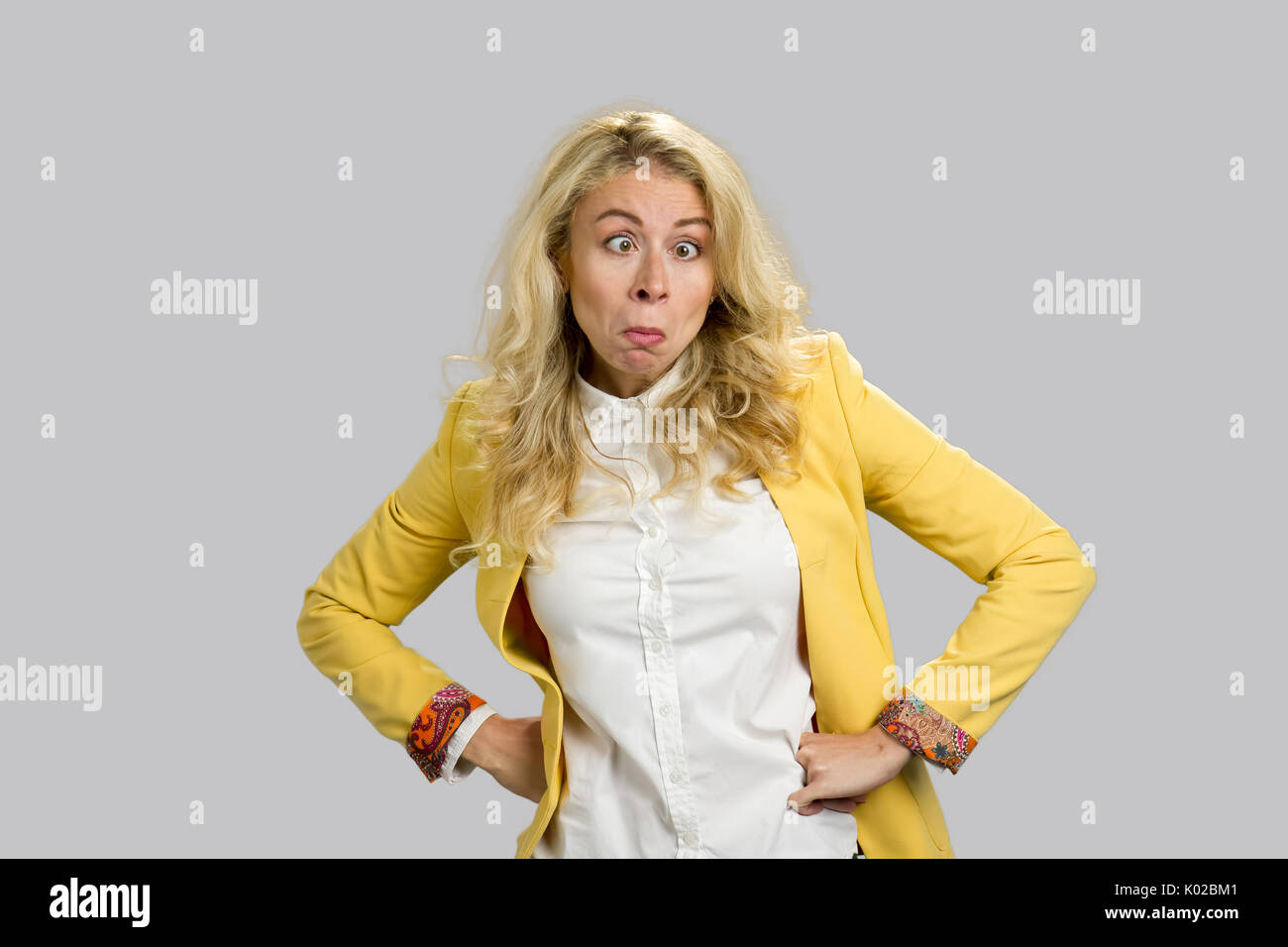 Überrascht Frau mit lustige Grimasse. Junge Geschäftsfrau mit Verblüffung überrascht lustiges Gesicht Ausdruck, Hände auf die Hüften auf grauem Hintergrund. Stockfoto