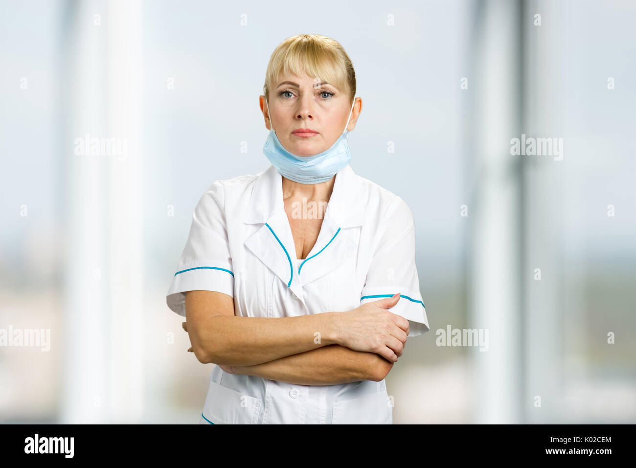 Portrait von Krankenschwester mit medizinischen Maske. Schwere reifen Arzt stehend mit medizinischen Maske unter dem Kinn auf verschwommenen Hintergrund. Stockfoto
