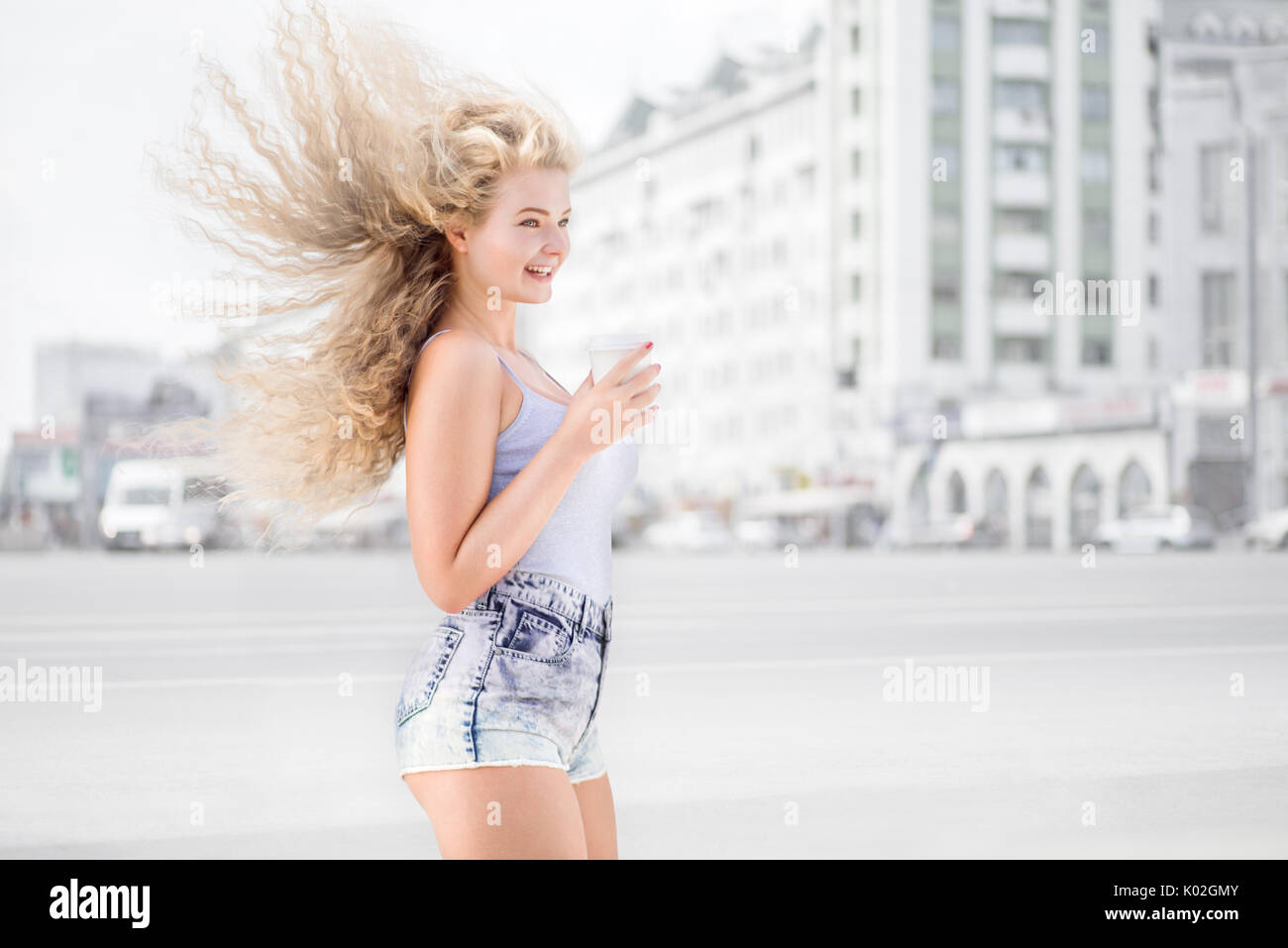 Glückliche junge Frau mit einer Tasse Kaffee zum Mitnehmen gegen urban Stadtverkehr Hintergrund. Stockfoto
