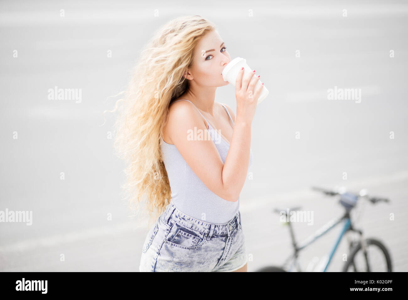 Glückliche junge Frau mit einer Tasse Kaffee nehmen und gegen leere Straße und City Bike Hintergrund. Stockfoto