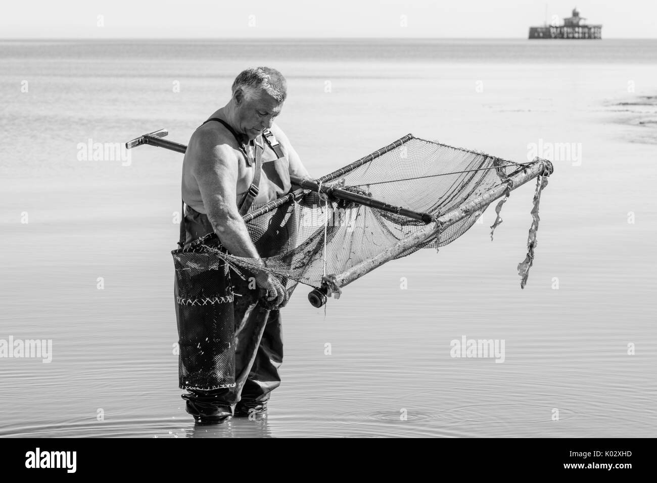 Fischer waders tragen mit einem Netz für den Fang von Garnelen in das Meer in Herne Bay, Kent. Im Hintergrund ist das Ende der alten Pier. Stockfoto