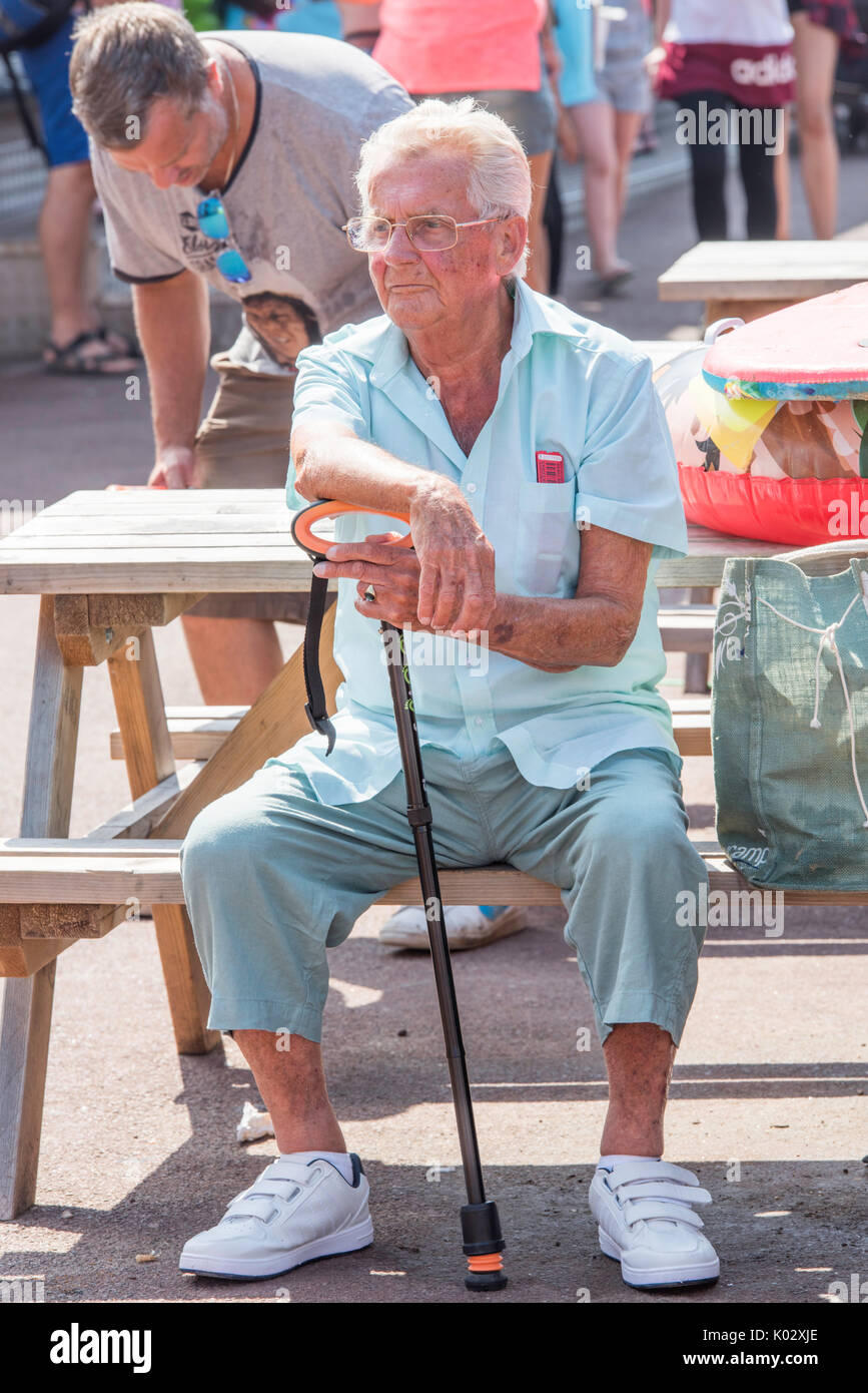Ältere Menschen sitzen auf einer Bank mit einem Gehstock in Dymchurch, Kent. Stockfoto