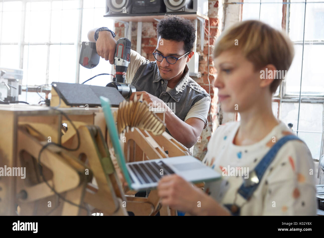 Designer mit Laptop und Bohrmaschine in der Werkstatt Stockfoto