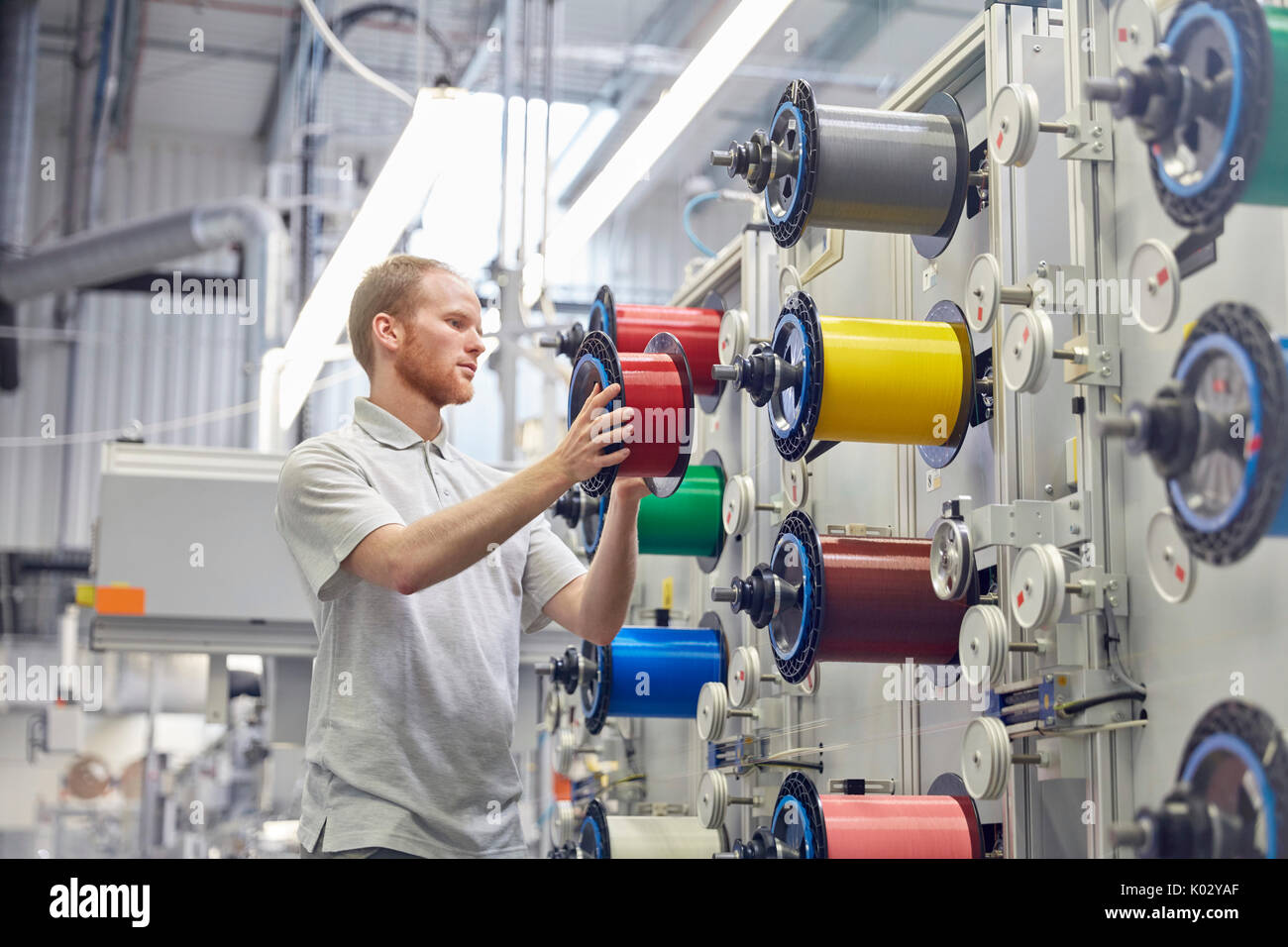 Männliche Arbeitnehmer ändern Spulen auf Maschinen in der Faseroptik Factory Stockfoto