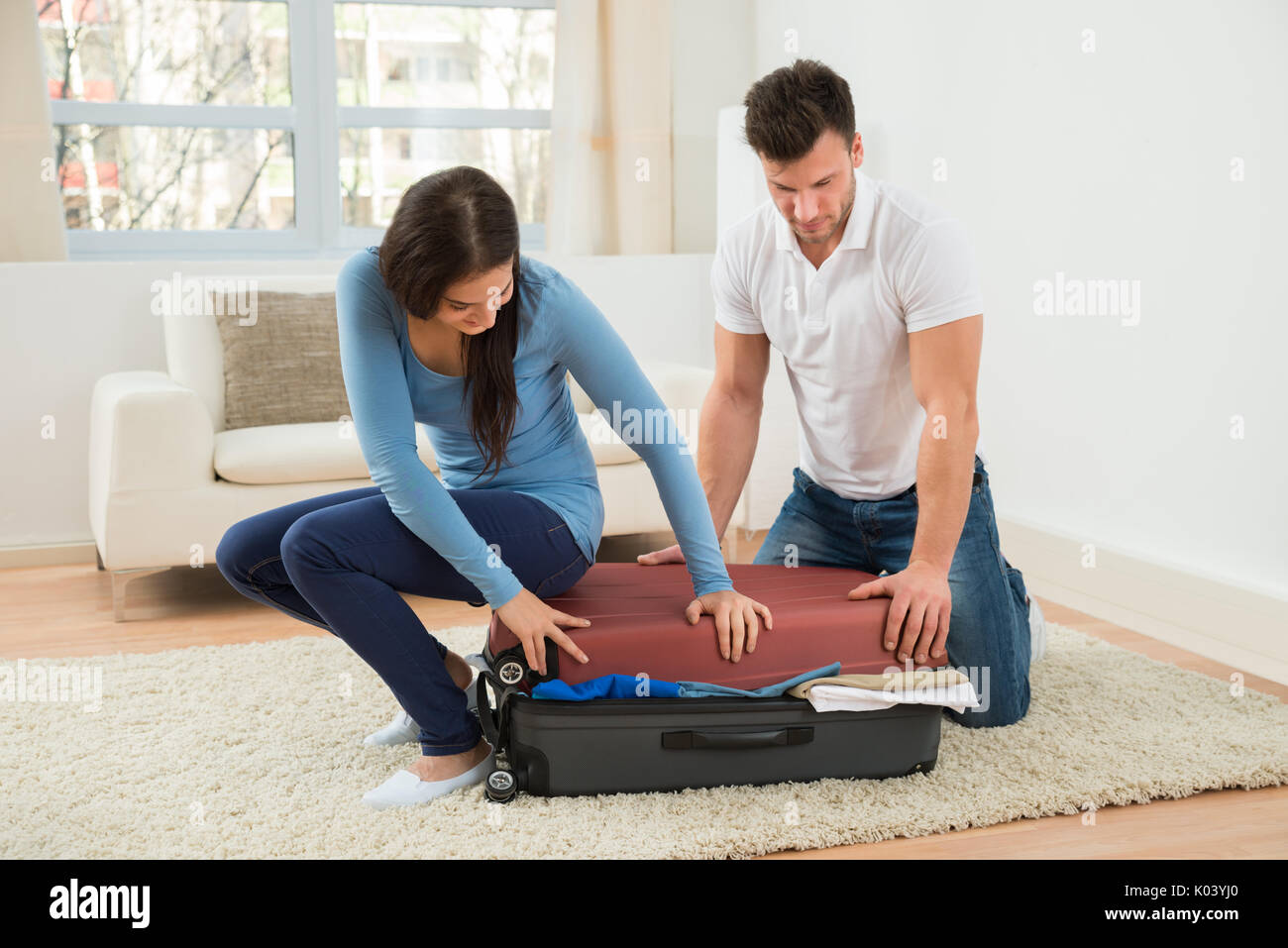 Junges Paar zu schließen Koffer mit viel Kleidung zu Hause versuchen, Stockfoto