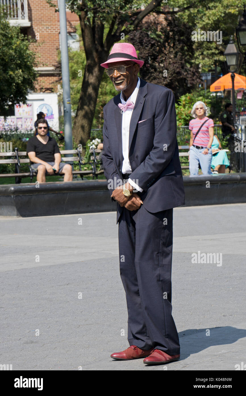 Ein gut gekleideter älterer Mann im Anzug mit einem rosa Hut, d Fliege und hankie beobachten Darsteller in den Washington Square Park in Manhattan, New York City Stockfoto