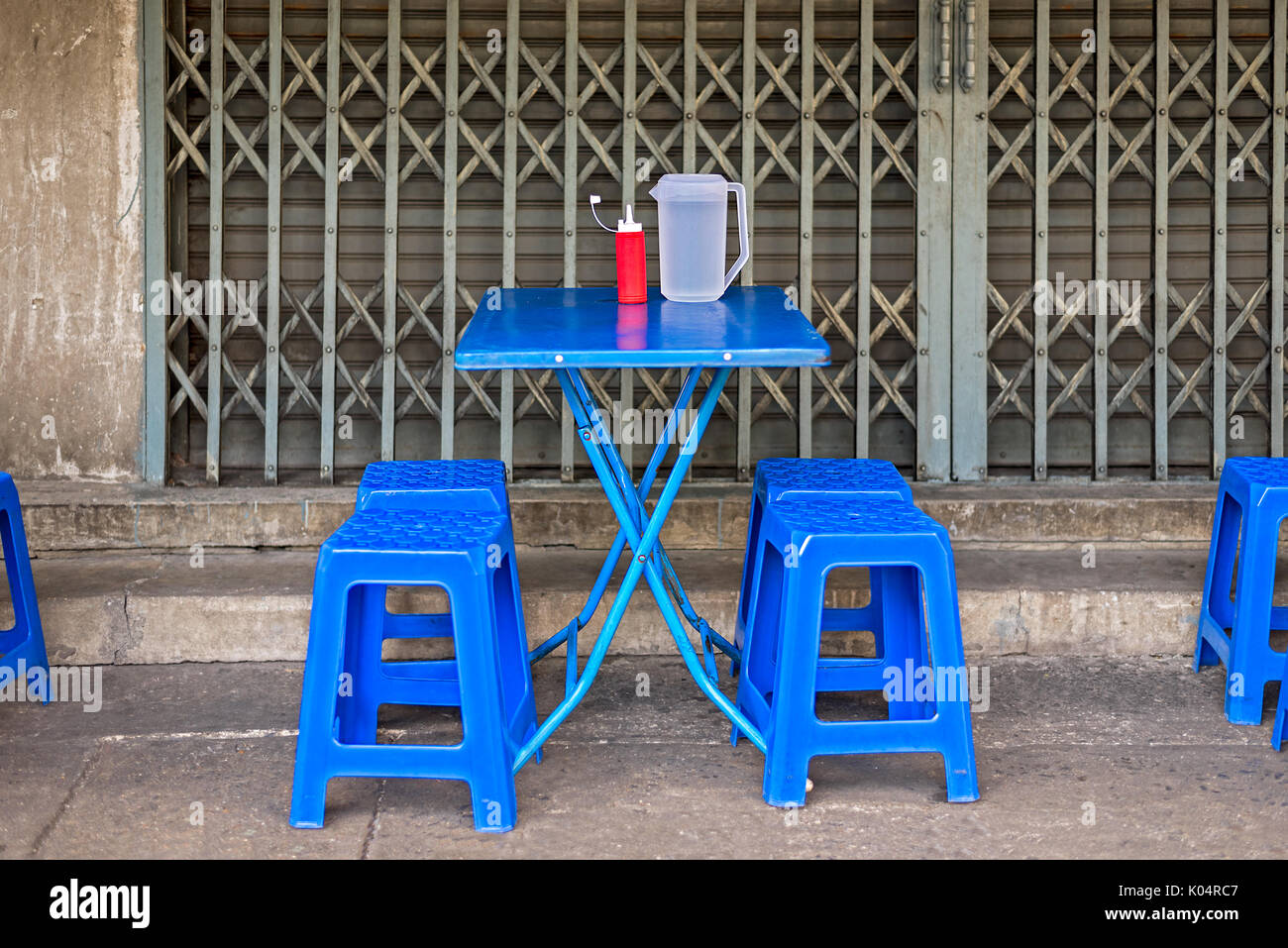 Asiatische Street Food Esstisch und Stühle auf dem Bürgersteig mit Wasser und Soße. Stockfoto