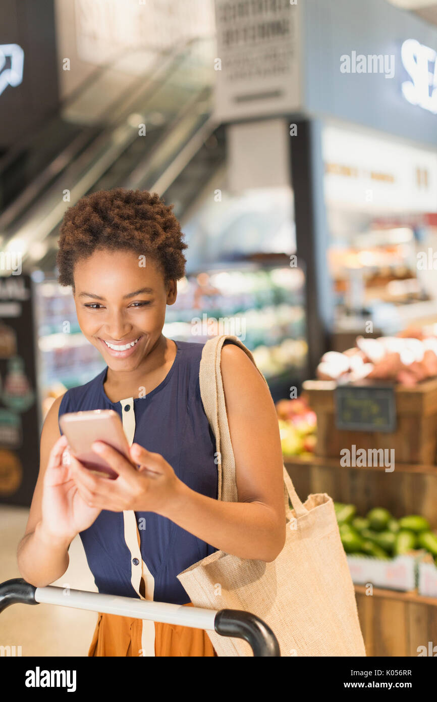 Lächelnde junge Frau mit Handy in Lebensmittelgeschäft Markt Stockfoto