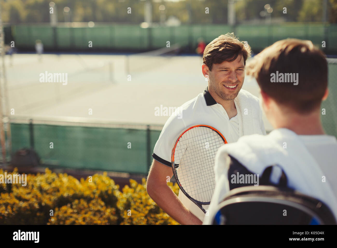 Jungen männlichen Tennisspieler sprechen über sonnige Tennisplätze Stockfoto