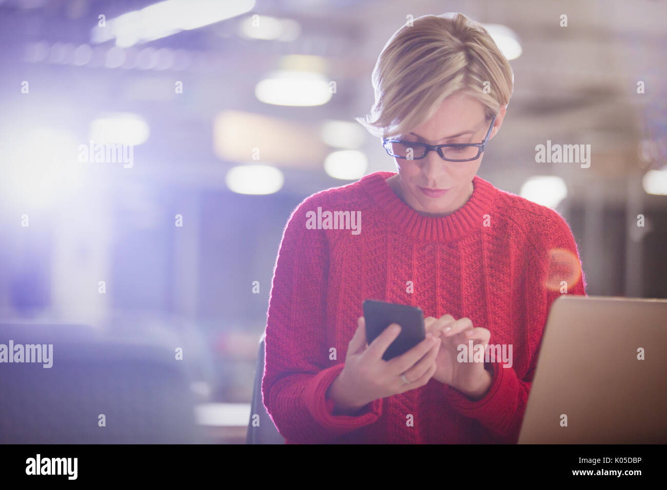 Geschäftsfrau, die spät am Laptop, SMS mit Handy in dunklen Büro Stockfoto