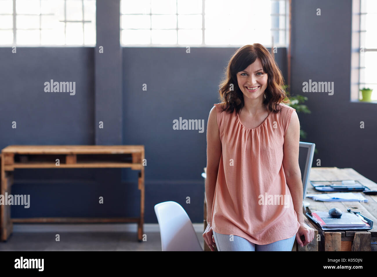 Lächelnden jungen Geschäftsfrau, lehnend auf einem Schreibtisch in einem Büro Stockfoto