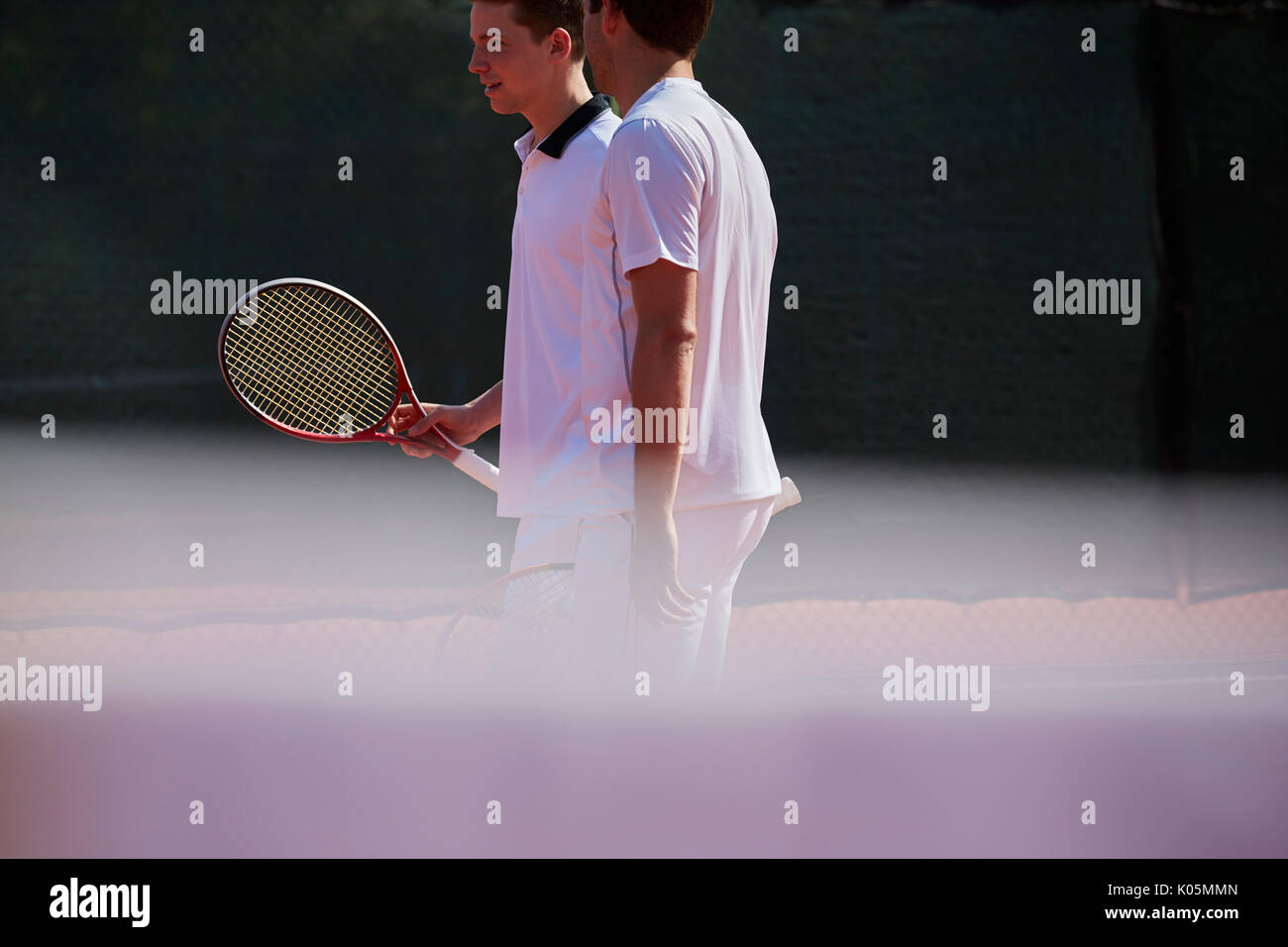 Männliche Tennis Doubles sprechen an sonnigen Tennisplatz Stockfoto