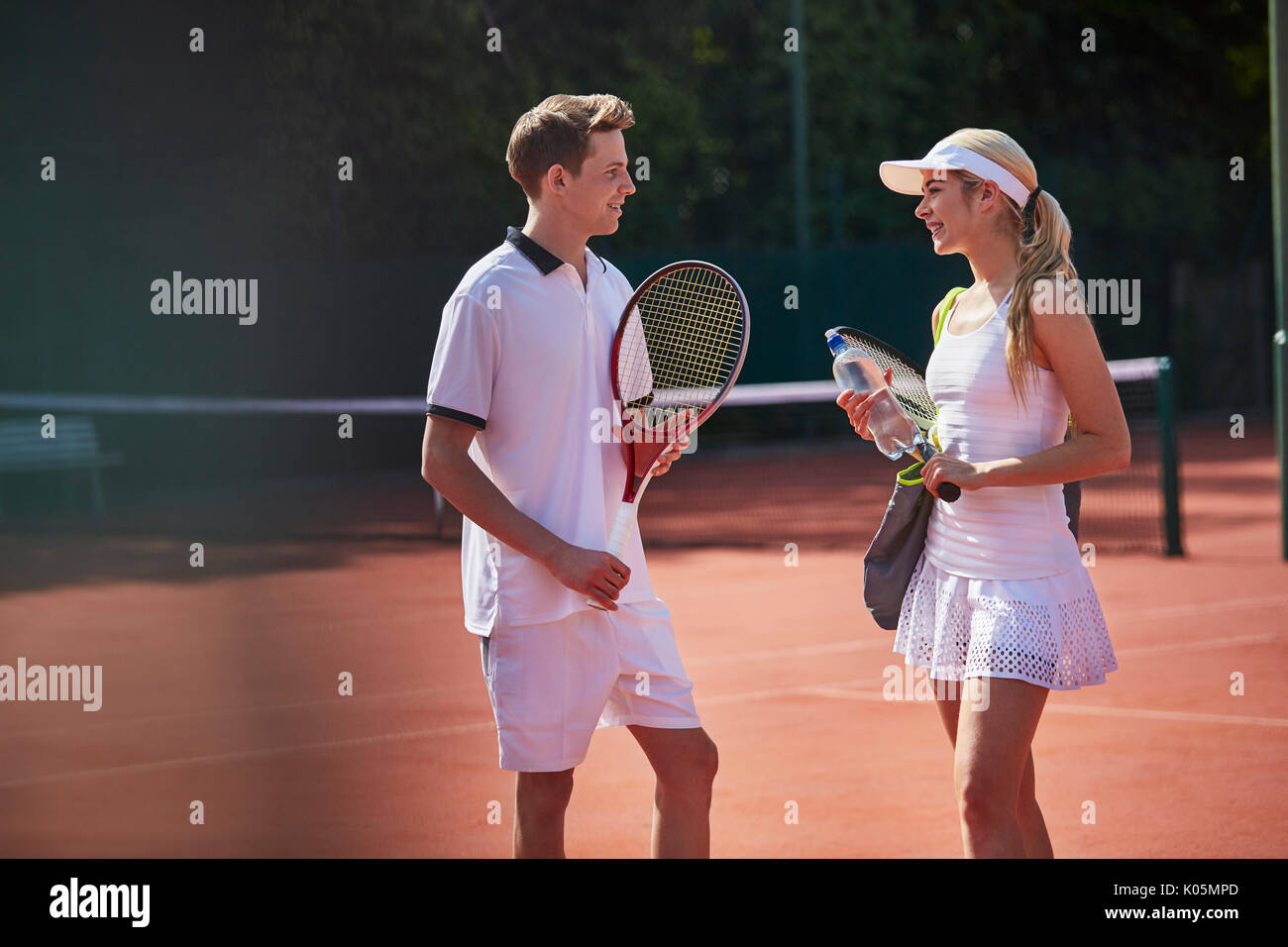 Männliche und weibliche Tennisspieler sprechen an sonnigen Tennisplatz Stockfoto