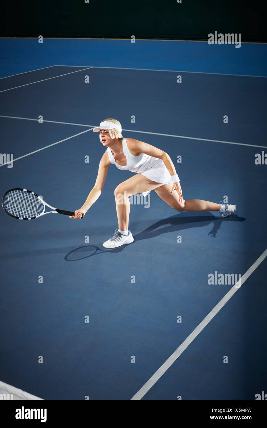 Junge weibliche Tennisspieler Tennis spielen, erreichen mit Tennisschläger auf Blau Tennisplatz Stockfoto