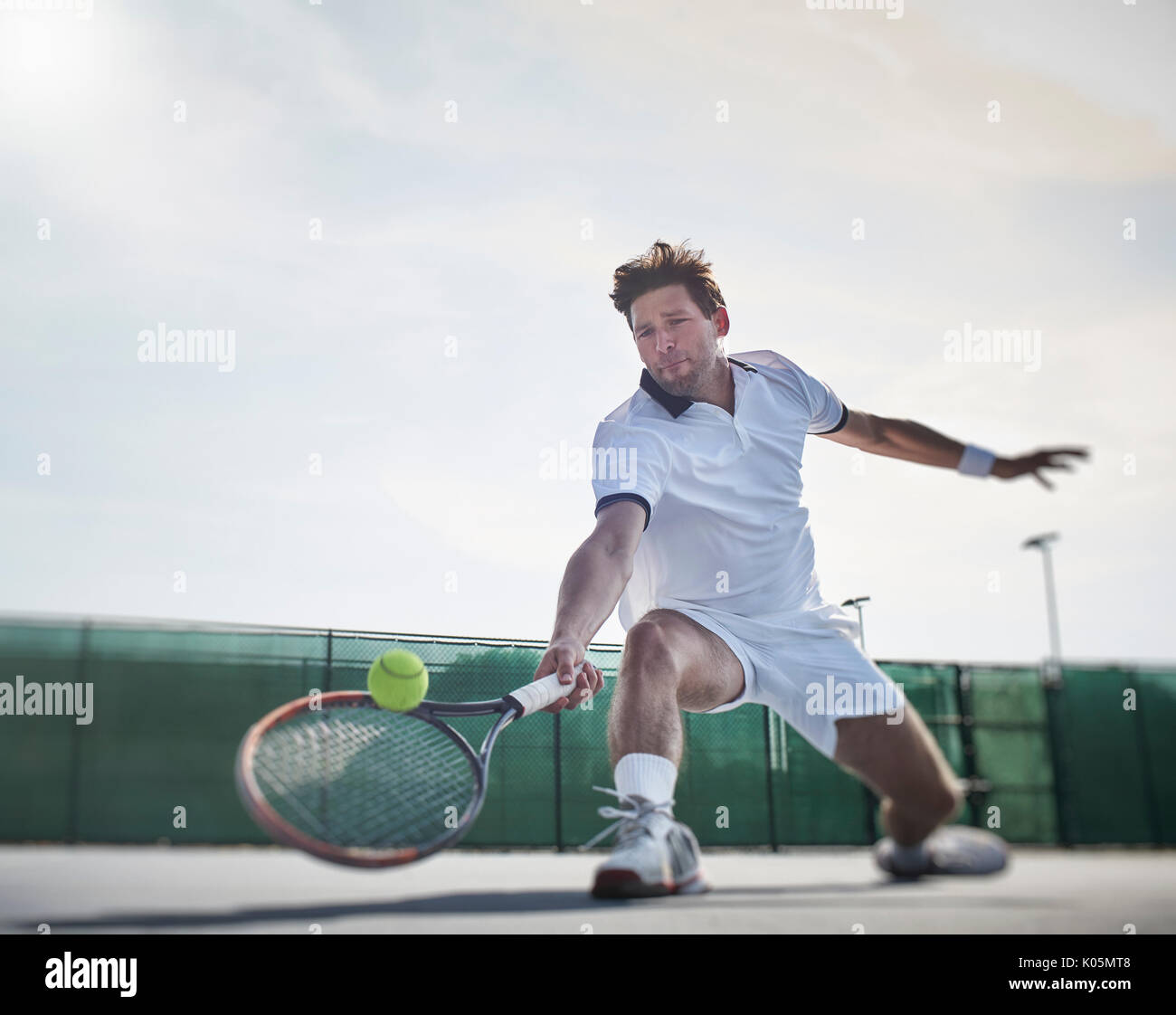 Entschlossene junge Mann tennis player Tennis spielen, erreichen für den Ball an sonnigen Tennisplatz Stockfoto