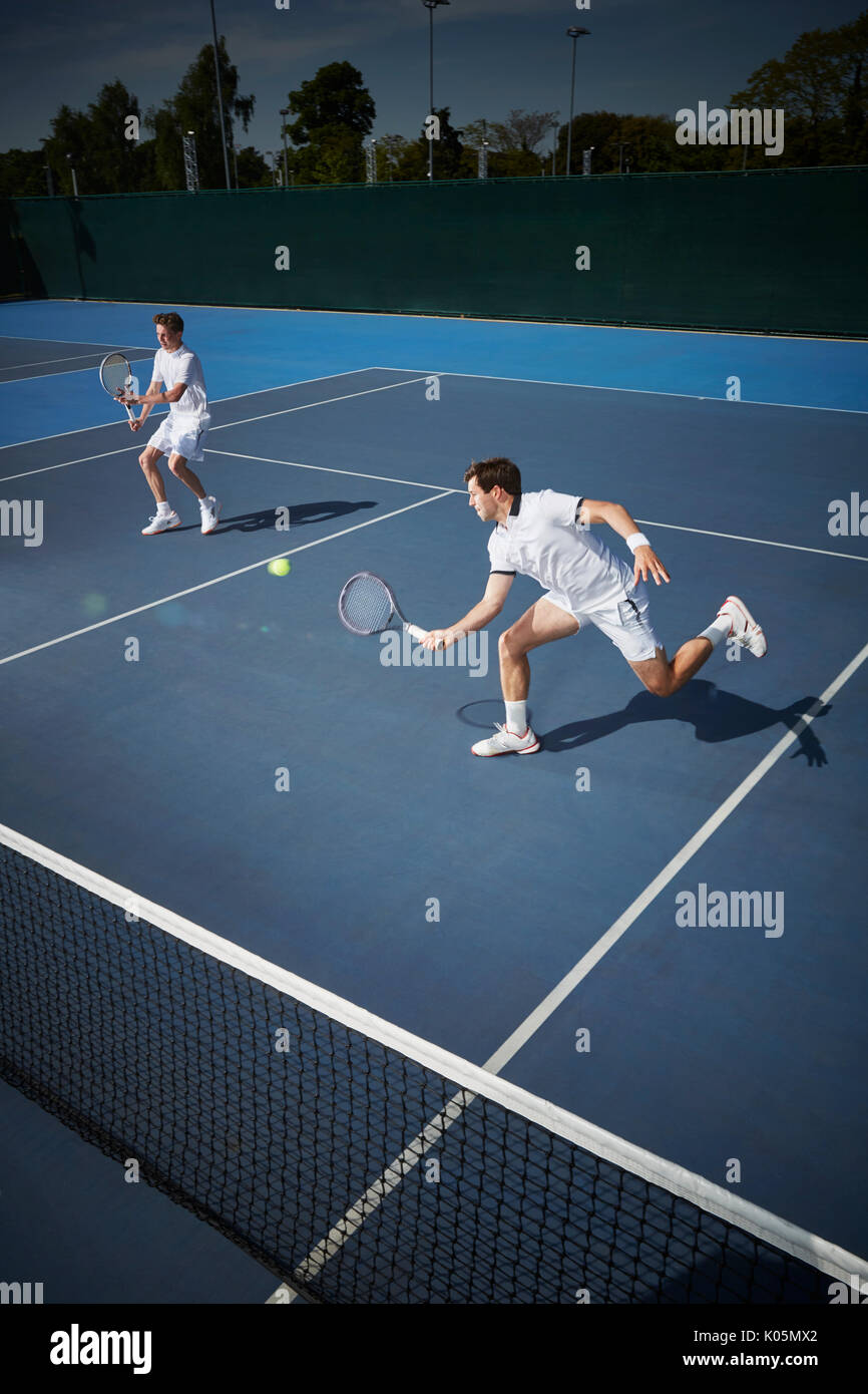 Junge männliche Tennis Doubles Spieler Tennis spielen, erreichen für die Kugel auf sonnigen blauen Tennisplatz Stockfoto