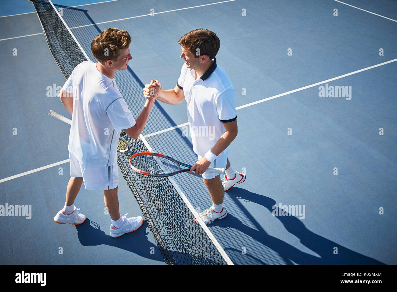Jungen männlichen Tennisspieler handshaking am Tennis net auf sonnigen blauen Tennisplatz Stockfoto