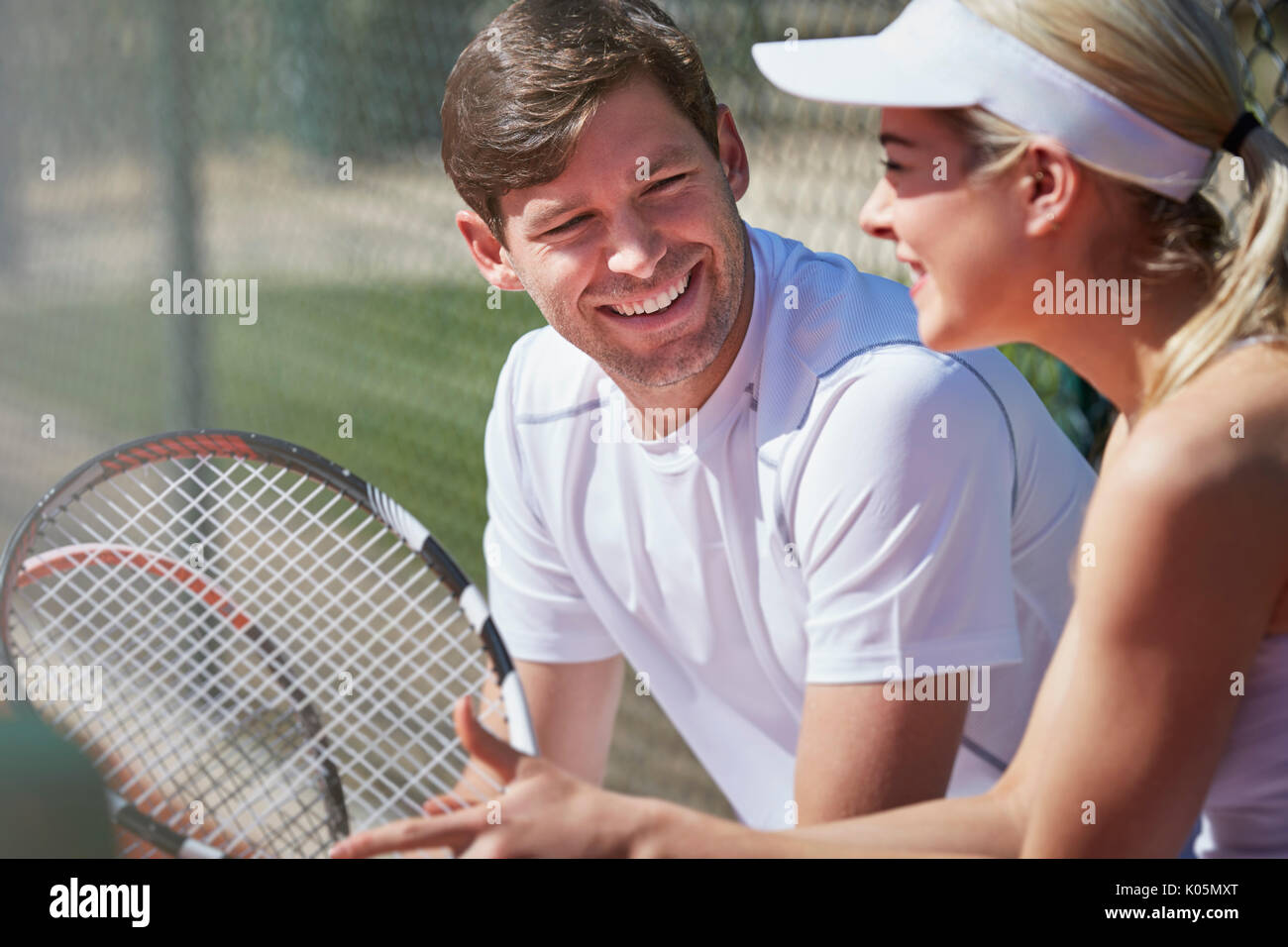 Lächelnd männliche und weibliche Tennisspieler ruhen und im Gespräch mit Tennisschläger im sonnigen Außenbereich Stockfoto