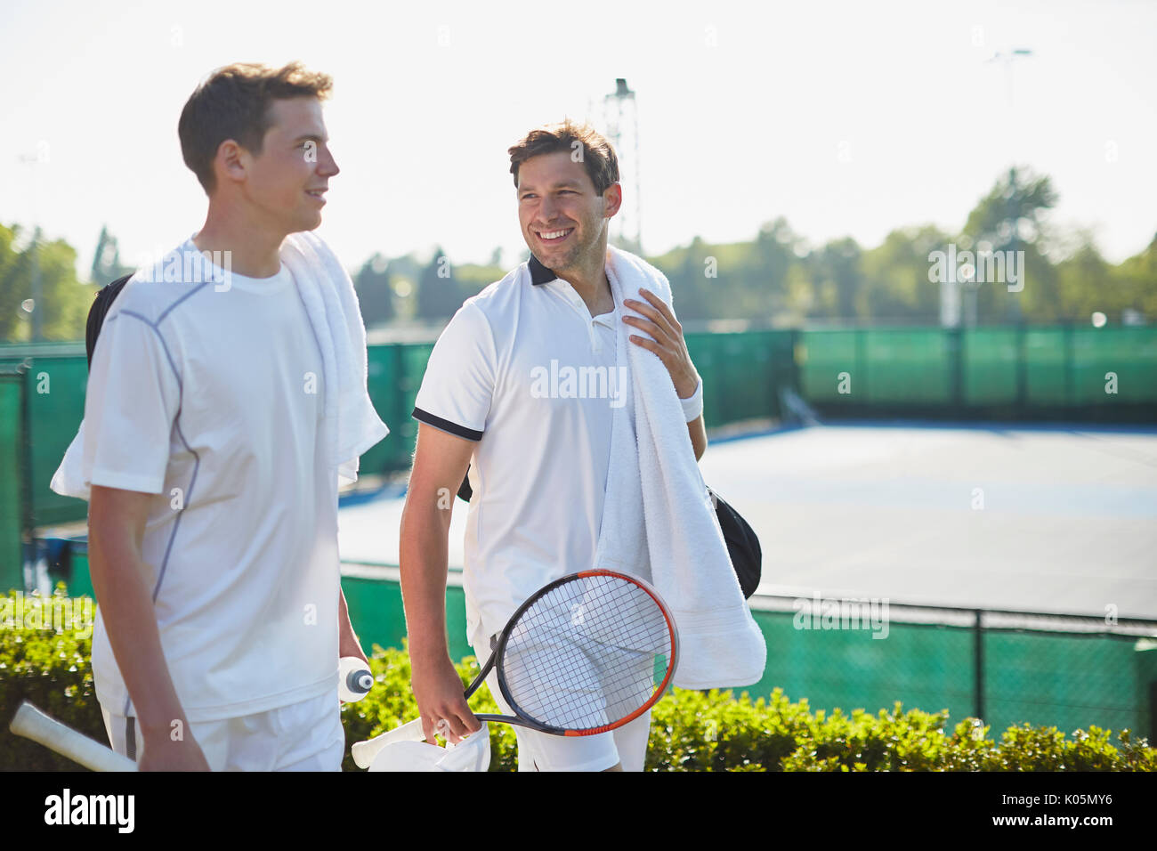 Lächelnden jungen männlichen Tennisspieler gehen mit Tennisschläger entlang sonnigen Tennisplatz Stockfoto
