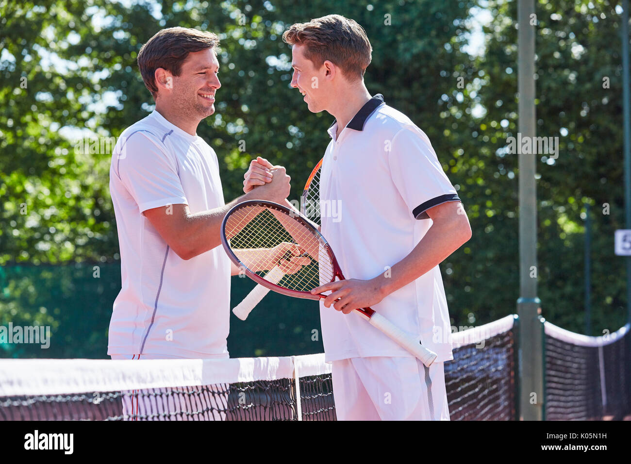 Lächelnden jungen männlichen Tennisspieler handshaking in sportsmanship über Netz auf dem Tennisplatz Stockfoto