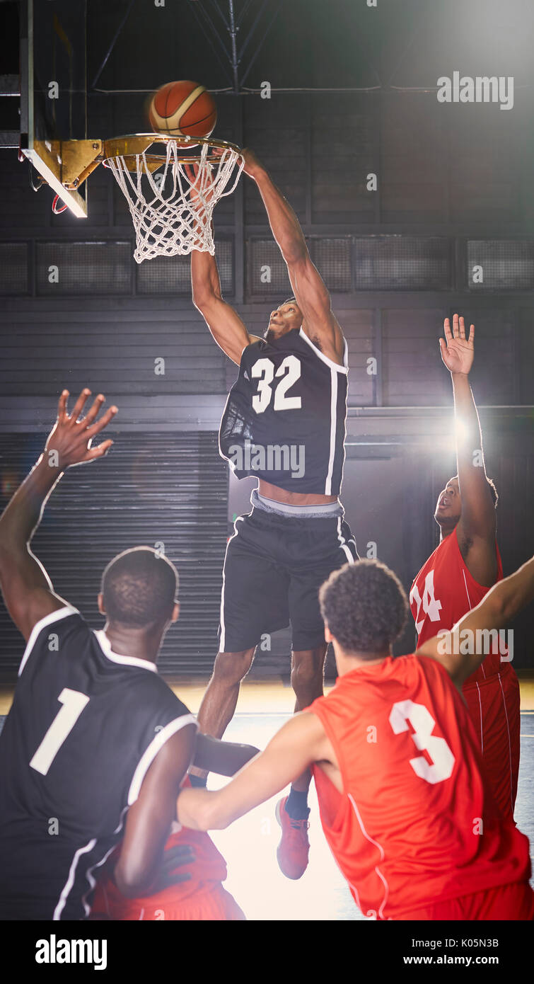 Junge männliche Basketball player Dunking den Ball in Hoop mit Verteidiger unter Stockfoto