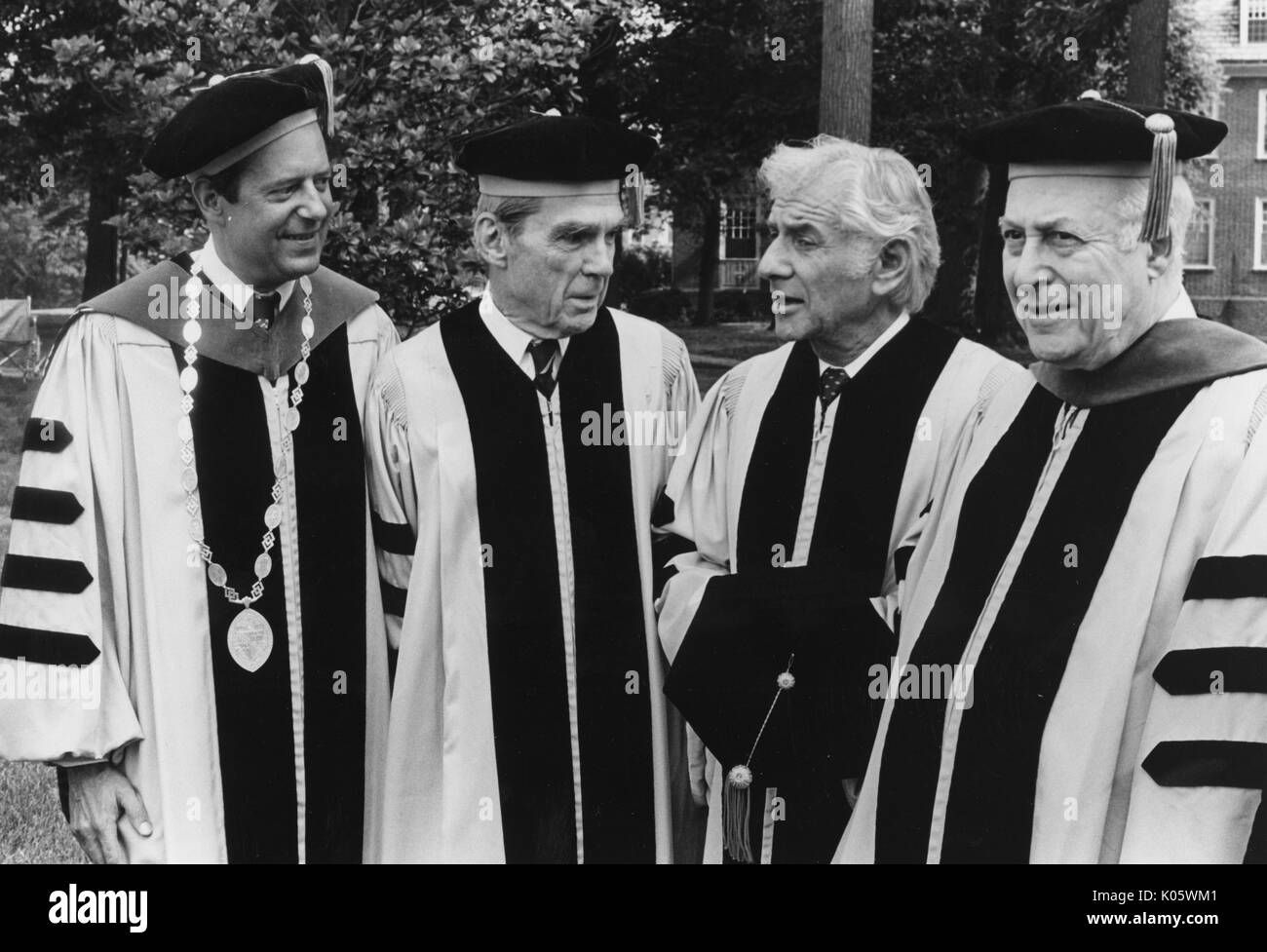 Brustbild von Von links nach rechts: Präsident Steven Muller, Professor Daniel K Ludwig, Musiker Leonard Bernstein, und Professor Milton Reder, in Gap und Kleid auf einem College quad für Johns Hopkins 1980 Beginn, 1980. Stockfoto