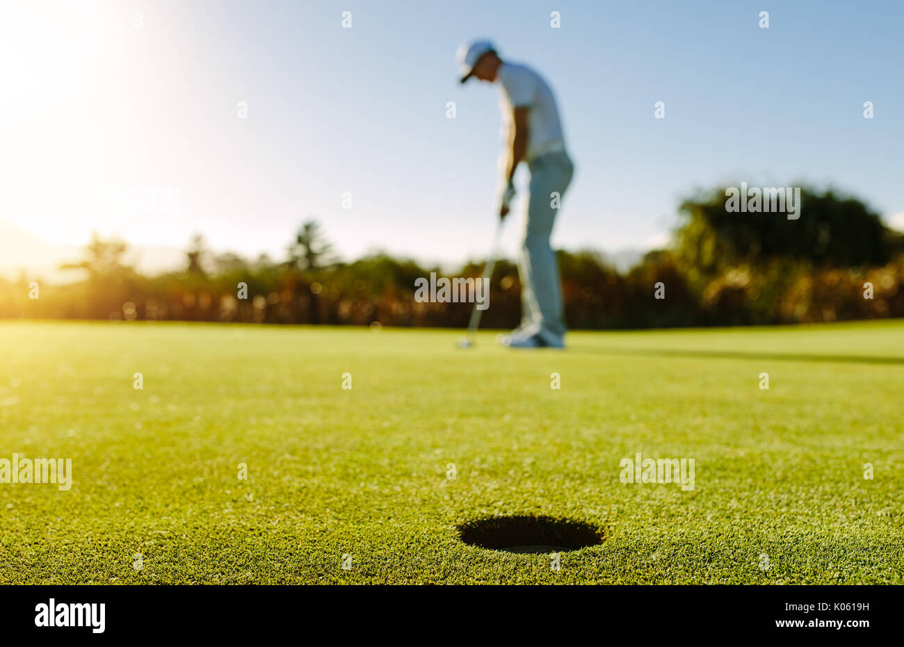 Golf Spieler die Kugel in Bohrung. Horizontale shot Golf Loch im grünen Feld mit Golfspieler im Hintergrund. Stockfoto