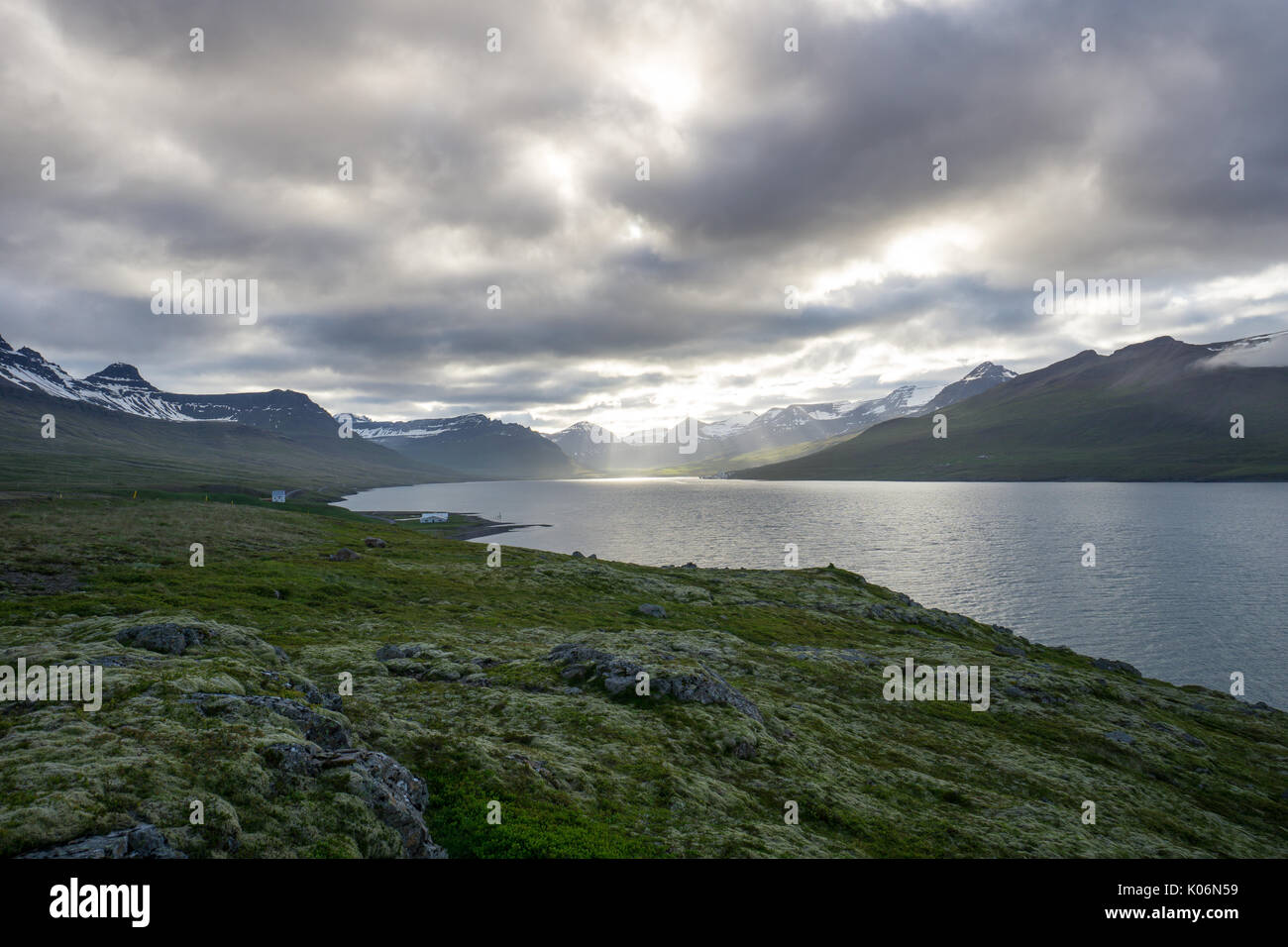 Island - Sonne bricht durch die Wolken am Fjord mit Bergen und grünen Moos bedeckte Landschaft Stockfoto