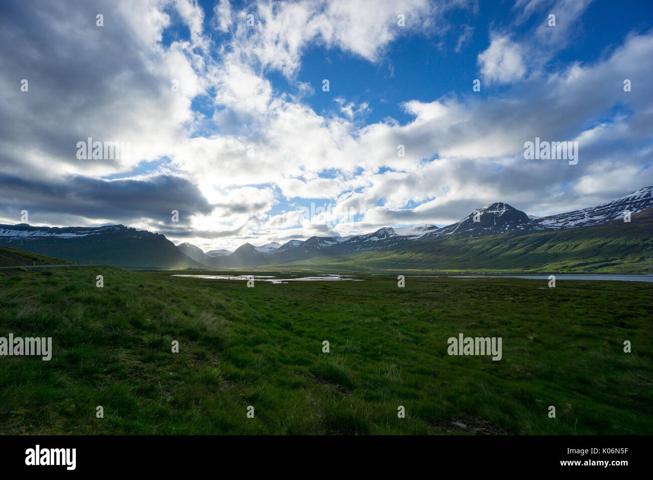 Island - Zauberhafte Landschaft, grüne Wiesen zwischen schneebedeckten Bergen im Sunshine Stockfoto