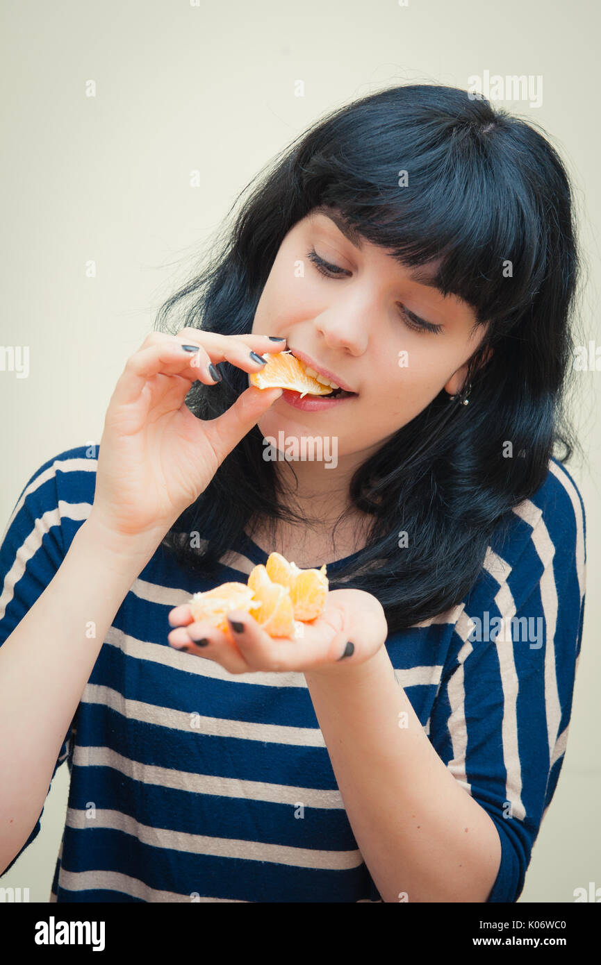 Lächelnde junge brünette Frau gerne Weinproben Orange Slice Portrait auf weißem Hintergrund Stockfoto