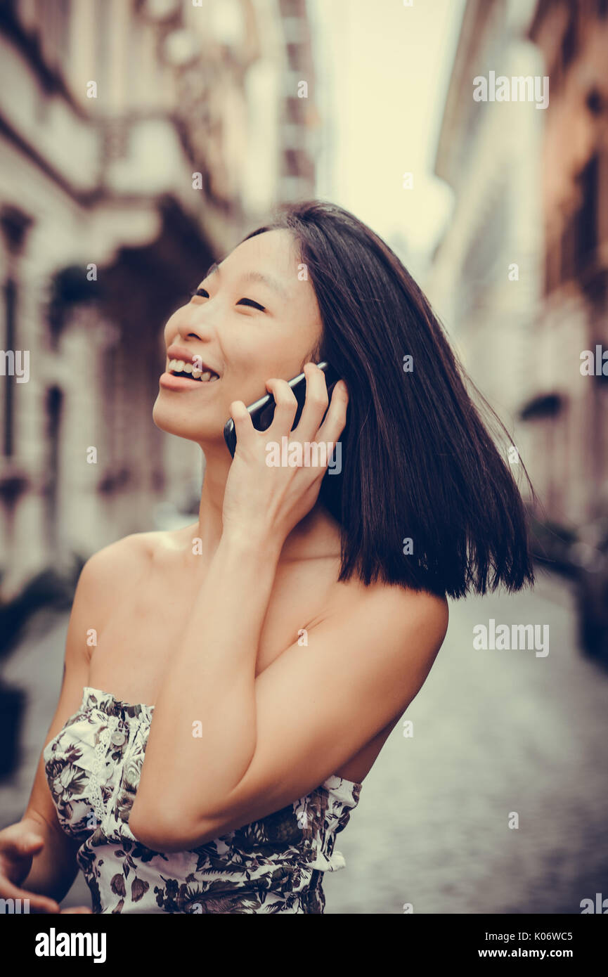 Junge schöne asiatische lächelnde Frau mit Handy auf der Straße Portrait auf der Suche Stockfoto