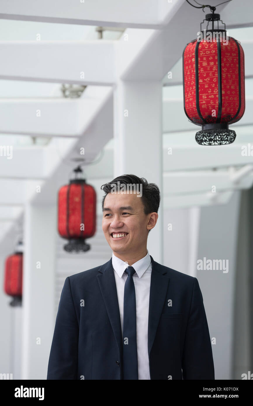 Chinesische Geschäft Mann in modernen asiatischen Stadt. Porträt eines asiatischen Geschäftsmann lächelnd und weg von der Kamera suchen, mit unscharfen Bürogebäude als Stockfoto