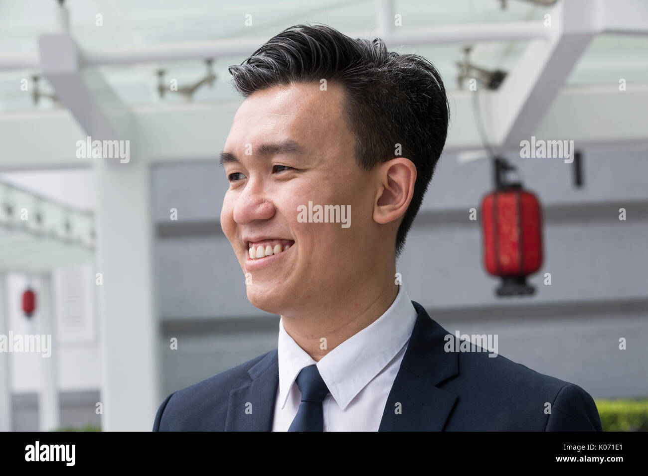 Chinesische Geschäft Mann in modernen asiatischen Stadt. Porträt eines asiatischen Geschäftsmann lächelnd und weg von der Kamera suchen, mit unscharfen Bürogebäude als Stockfoto