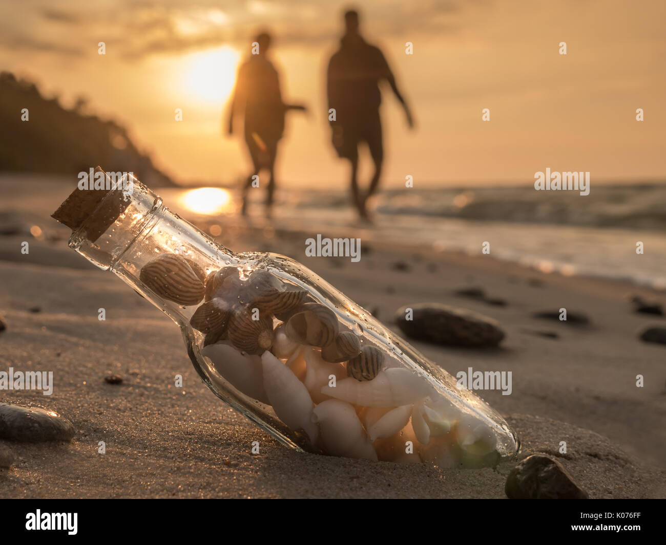 Flasche mit Korkgeschmack mit Muscheln im Sand stecken am Strand gegen den Sonnenuntergang Stockfoto