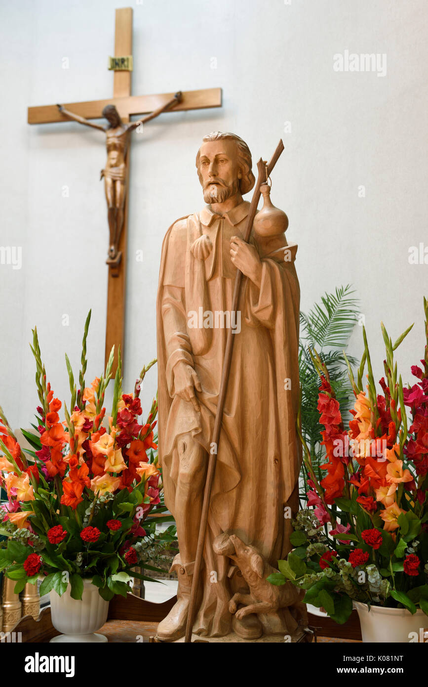 Eine hölzerne Statue der Heiligen Rochus mit Pest bubo auf den Oberschenkel und Hund mit Brot, der ihn in der Katholischen Kirche Heiligtum mit Kruzifix gespeichert Stockfoto