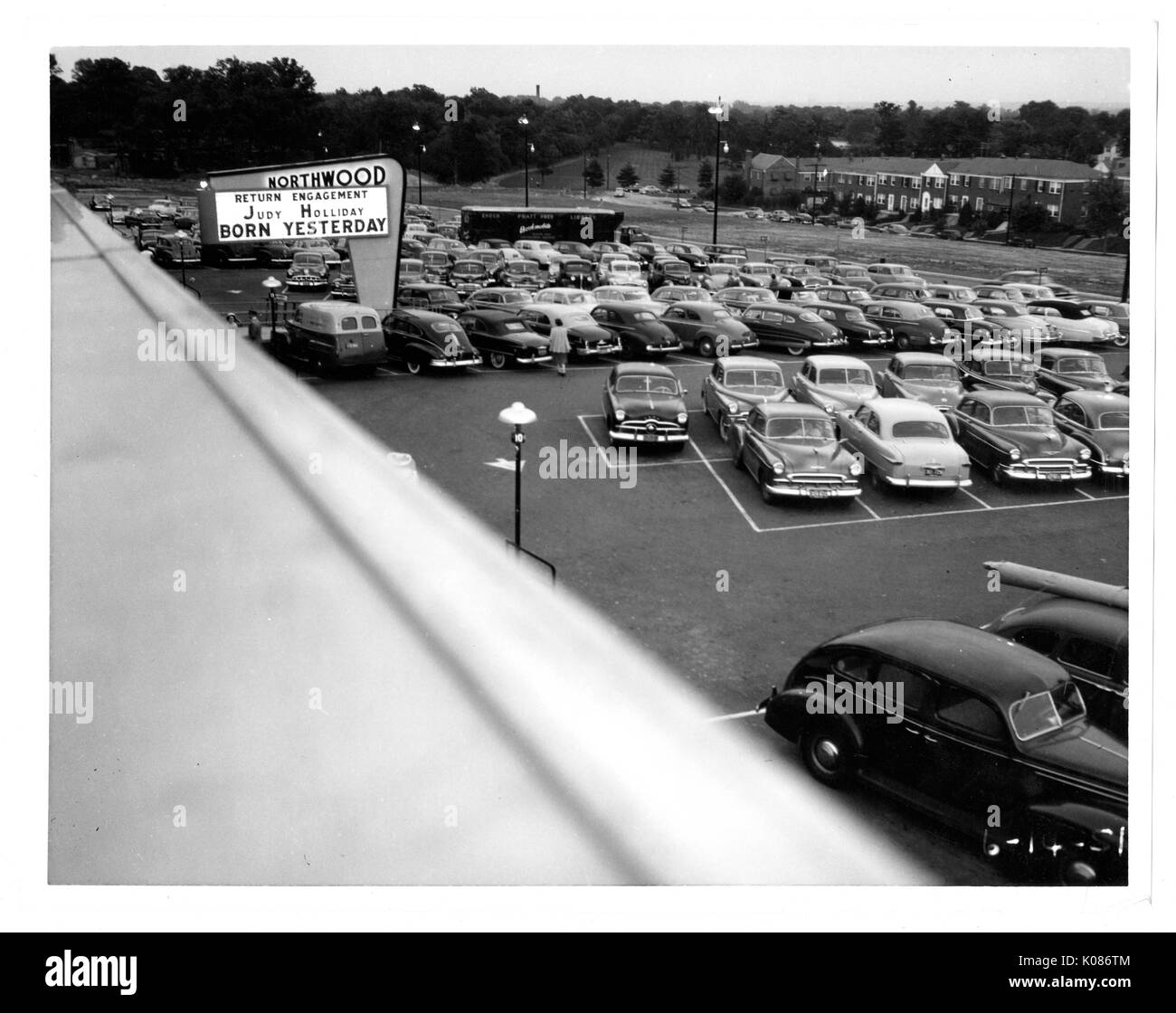 Foto geschossen oberhalb der Northwood Einkaufszentrum Parkplatz in Baltimore, mit Autos gefüllt, von einem beleuchteten Schild mit der Aufschrift "Northwood", mit vielen Bäumen int er Hintergrund, jedes Auto ordentlich in die weißen Linien, dass jeder Raum abgrenzen, Baltimore, Maryland, 14. Juni 1951 abgestellt. Stockfoto