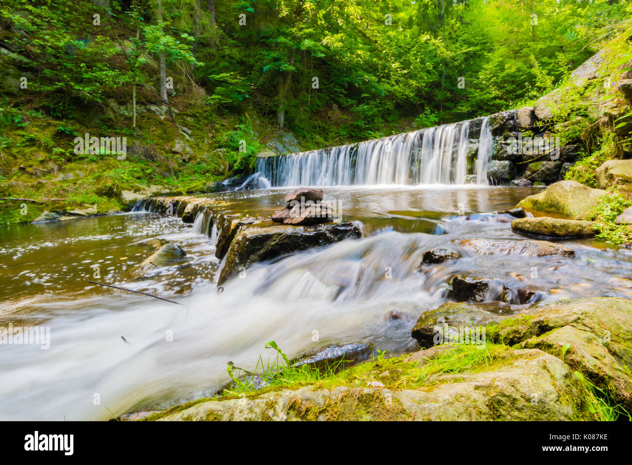 Schöne kleine Wasserfall auf der schönen Bach im Wald in der Tschechischen. Lange Belichtungszeit, milchiges Wasser Effekt, Bäume und grüne Gras um, Felsen und Steine Stockfoto