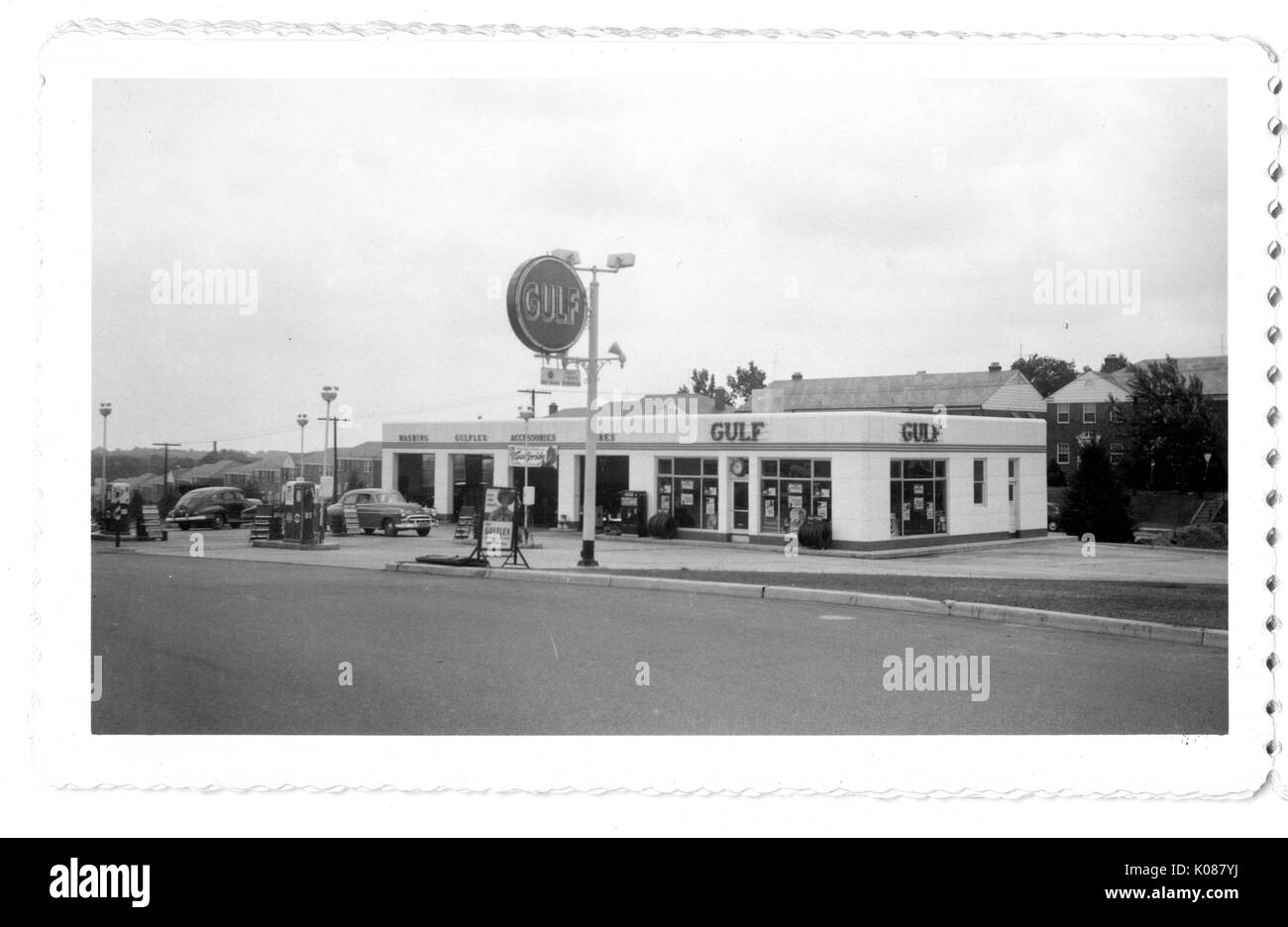 Blick über die Straße der Gulf Tankstelle, Golf ist auf dem Gebäude der Werbung sowie auf ein großes Schild Treiber anzuziehen, die Tankstelle ist in hellen Farben gestrichen und zwei Automobile erhalten Service, Baltimore, Maryland, 1951. Stockfoto