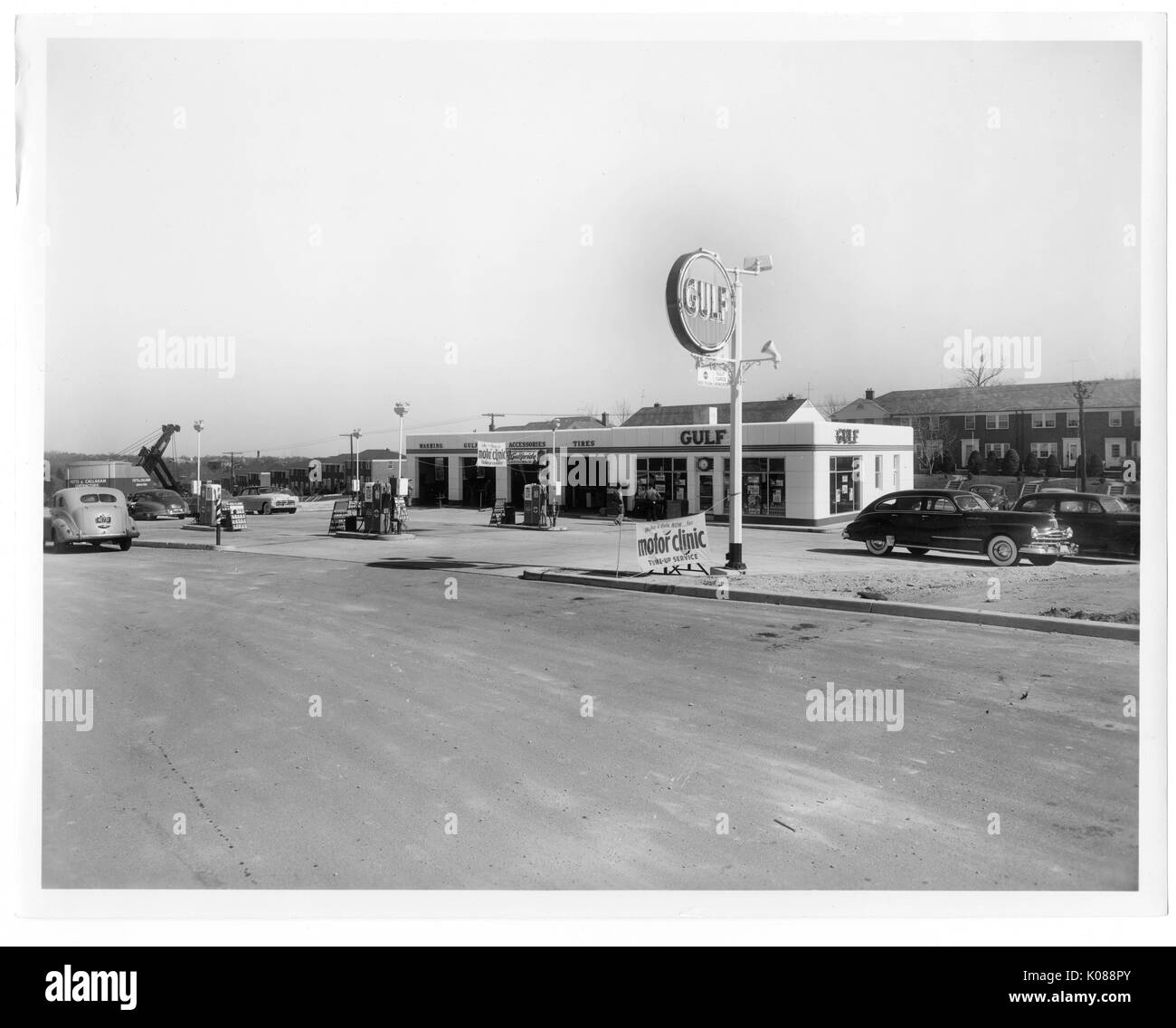 Blick über die Straße der Gulf Tankstelle, Golf auf dem Gebäude geworben wird, sowie auf ein großes Schild Treiber anzuziehen, die Tankstelle ist in hellen Farben gestrichen, Reihe Wohnungen an der Rückseite der Station, Baltimore, Maryland, 1951. Stockfoto